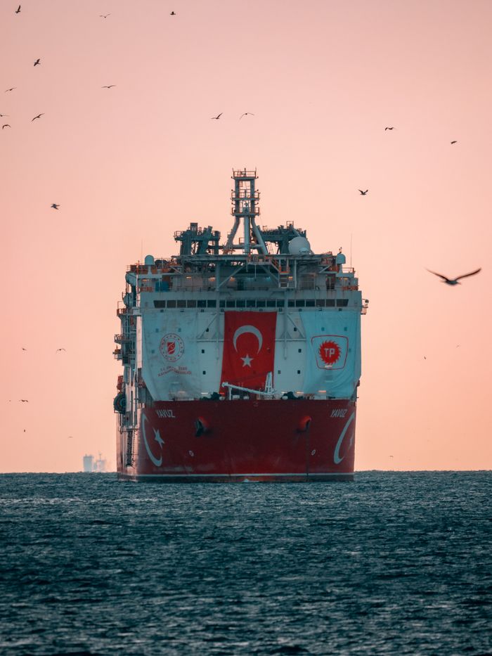 A Turkish oil tanker sails on the sea with birds flying overhead at sunset.